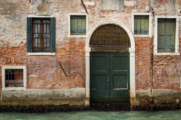 Entrance in an old brick wall near water in Venice (Italy), cloudy day in autumn
