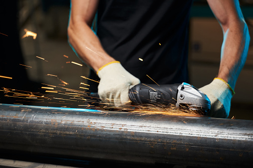 an angle grinder in male hands in gloves grinds a pipe with sparks. High quality photo