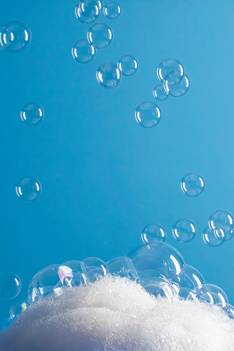 A DSLR photo of soap sud with bubbles flying on a blue background.