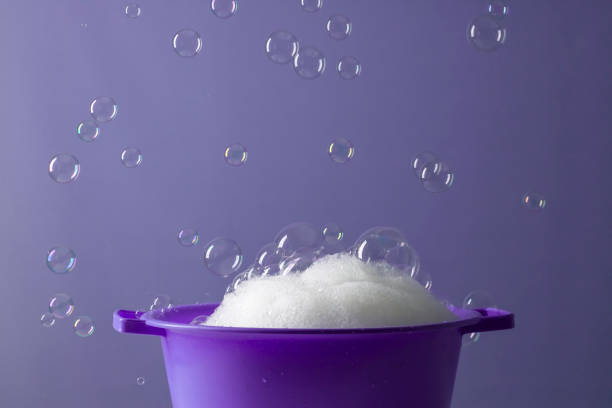 A DSLR photo of soap sud in a bowl with bubbles flying on a purple background.