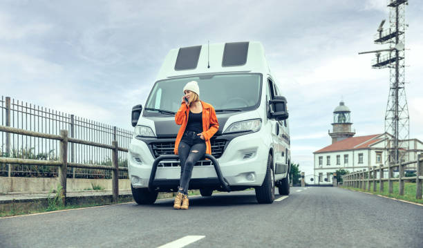 Woman leaning on camper van on the road calling by mobile