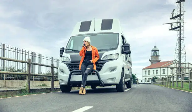 Photo of Woman leaning on camper van on the road calling by mobile