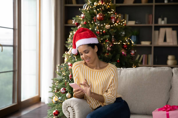 istock Relaxed young mixed race woman using cellphone near Christmas tree. 1351285347