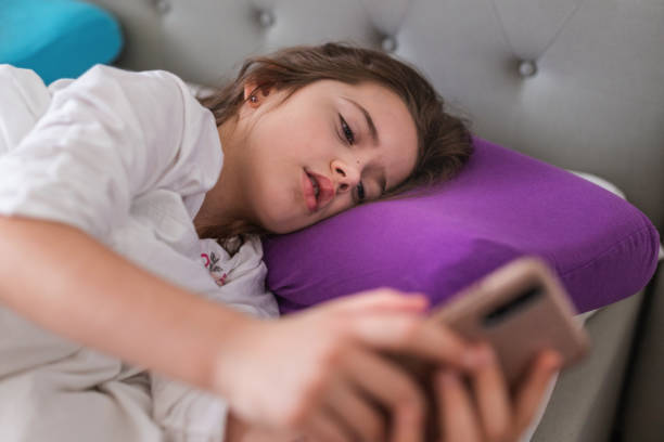 istock Serious young girl using mobile phone in bed 1351285417