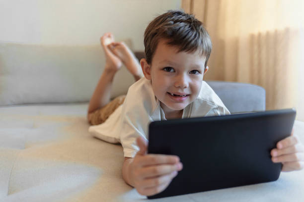 istock Cute Caucasian boy watching cartoons while lying on front in bed at home. 1351289719