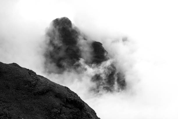 Black and white of a lone Mountain Peak, peeking out between the thick fog in the Drakensberg Mountains of South Africa, giving the illusion that it is floating. These cliffs and peaks were formed due to the combination of the Jurassic period large flood basalt during the break-up of the Gondwana Supercontinent and erosion due to the later uplift of the African Continent. The photo was taken in an area at the border between South Africa and Lesotho