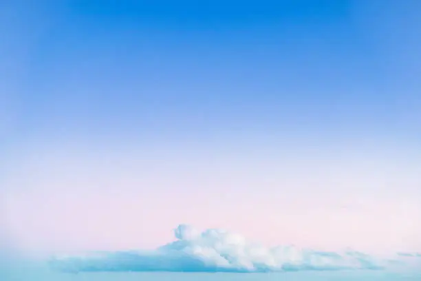 A single, large cumulus cloud, low on the horizon at sunset, with soft graduated blue and pink colours in the sky above it.