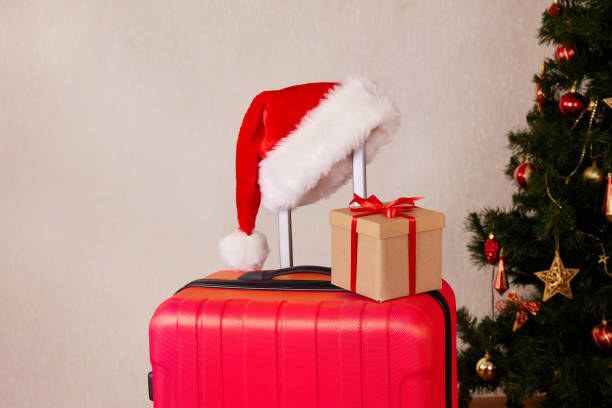 A red suitcase, a Santa Claus hat and a gift box. The concept of traveling for Christmas. A red suitcase, a Santa Claus hat and a gift box. The concept of traveling for Christmas. Copy space. unmanned spacecraft stock pictures, royalty-free photos & images