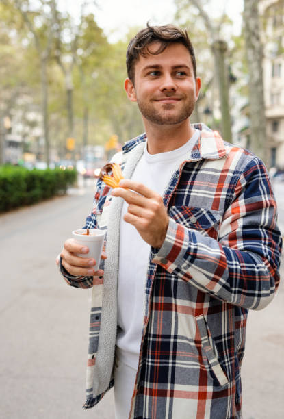 istock Cheerful man eating churros with chocolate in city 1351299447