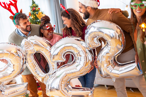 Group of young friends having fun celebrating New Year at home, holding giant balloons shaped as numbers 2022