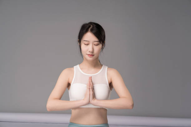 若くて美しいアジアの女性、ヨガパンツとスポーツ下着を着て、ヨガを練習し、灰色の背景 - 心と身体を整える ストックフォトと画像