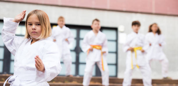 Schoolgirl training karate at schoolyard with friends Portrait of european preteen girl practicing karate on a street near school on sunny day schoolyard fight stock pictures, royalty-free photos & images