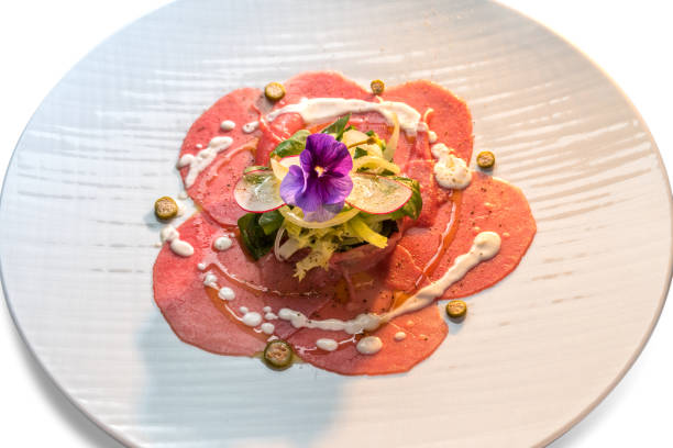 Raw beef carpaccio Raw beef carpaccio, Slices of raw veal fassone meat with salad, radishes, capers and violet flower edible in white dish carpaccio parmesan cheese beef raw stock pictures, royalty-free photos & images