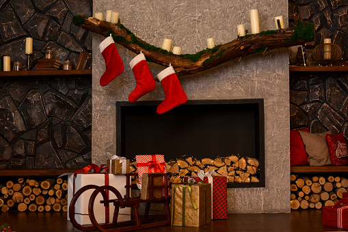 Christmas boxes with gifts in a sled against the background of a fireplace and hanging Santa's socks. Christmas mood, Christmas interior