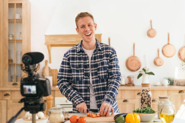 istock Young man, a chef looking at the camera, filming himself for a culinary blog, preparing a healthy meal with vegetables in the kitchen 1351316680