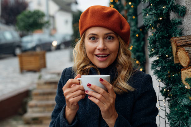 портрет улыбающейся женщины, наслаждающейся чашкой чая, сидя в кафе на открытом воздухе - mature women portrait hat human face стоковые фото и изображения