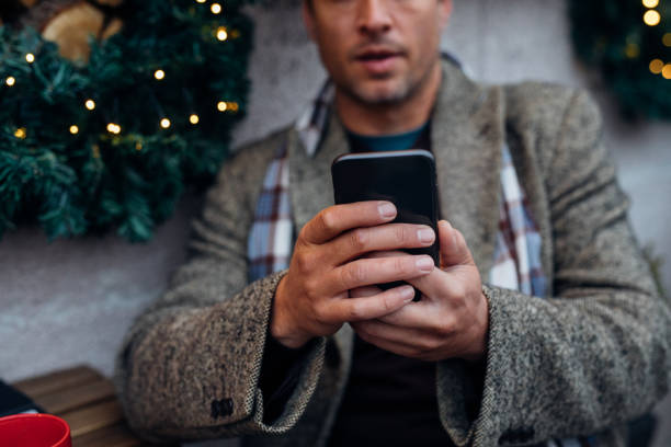 фото крупным планом руки мужчины, использующего мобильный телефон в кафе на открытом воздухе - people winter urban scene chair стоковые фото и изображения