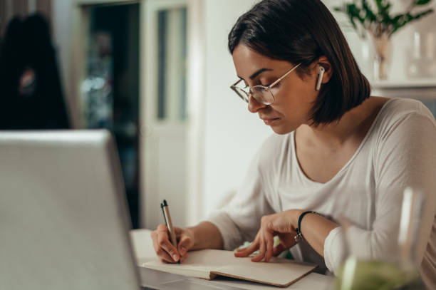 istock Woman writing in a notebook and using a laptop while working from home 1351317500