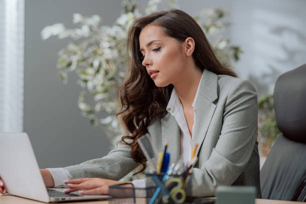 Focused on work attractive pretty brunette girl in classic makeup wearing a shirt and jacket, sits at a desk in a company in front of a laptop, fills out documents, reads email, answers messages enfocado en el trabajo atractiva chica morena bonita con maquillaje clásico con camisa y chaqueta, se sienta en un escritorio en una empresa frente a una computadora portátil, llena documentos, lee correos electrónicos, responde mensajes