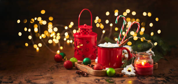 red cup of hot cocoa with marshmallows and candy canes on wooden table with christmas tree and glowing garland for christmas - julfika bildbanksfoton och bilder