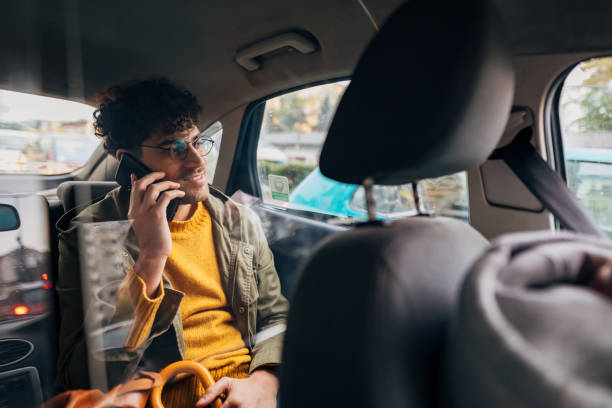 istock A handsome young man is talking on a mobile phone in the back seat. About 25 years old, smiling white man with eyeglasses. 1351319316