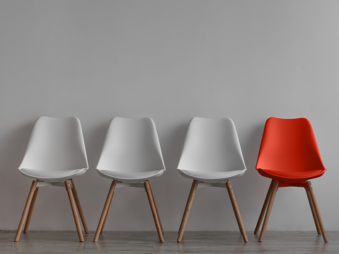Tres sillas blancas vacías y una roja sobre fondo de pared gris en oficina o habitación photo