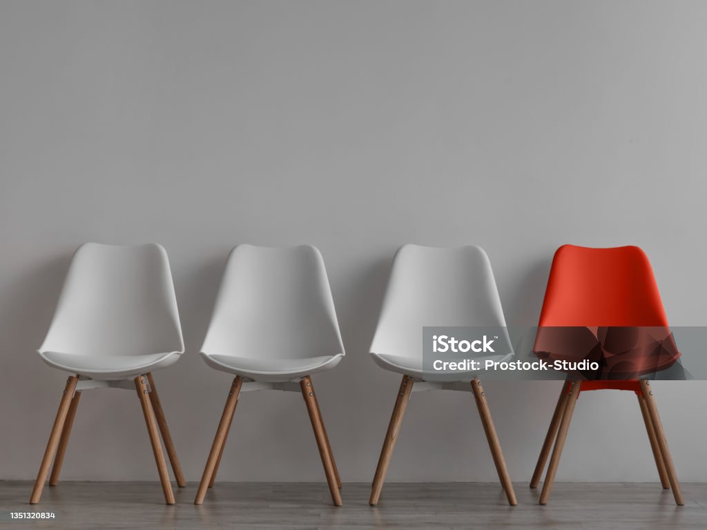 Three vacant white chairs and one red on gray wall background in office or room Three vacant white chairs and one red on gray wall background in office or room. Simple minimalist interior, nobody, free space. Job recruiting, leadership and business due covid-19 virus, mockup Chair Stock Photo