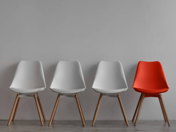 Three vacant white chairs and one red on gray wall background in office or room Three vacant white chairs and one red on gray wall background in office or room. Simple minimalist interior, nobody, free space. Job recruiting, leadership and business due covid-19 virus, mockup chair stock pictures, royalty-free photos & images