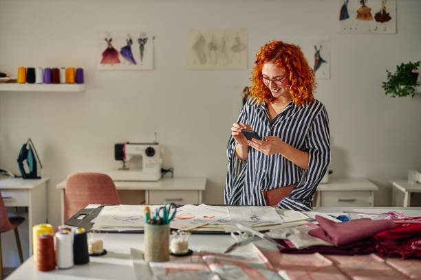 istock Ginger female worker using phone in fashion studio 1351322375