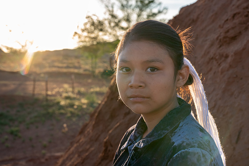 Twelve Year Old Native American Navajo Girl Looking seriously at the camera in front of a traditional Indian hogan at the Monument Valley Tribal Park at the Arizona/Utah Border in the United States