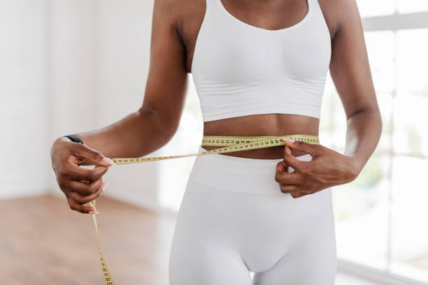 чернокожая женщина измеряет талию скотчем. диета для похудения конце пция - похудение стоковые фото и изображения