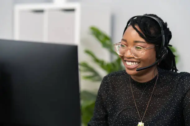 Photo of Customer service agent, financial advisor call center employee sits at desk in company in front of computer screen, headphones with microphone on ears, connecting with caller, solving problem
