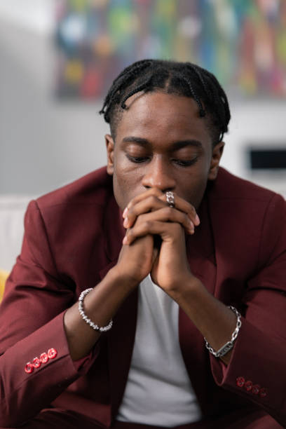 istock Dark skinned man with dreadlocked wearing smart suit sitting in office hands resting on knees joined in front of face worry sadness pondering company problems money troubles thinking of solution 1351326098