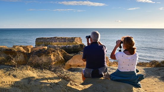 Costa da Caparica, Algarve - 3 November 2021: Couple with binoculars watching sea birds on the rocks, Algarve coast, Portugal, Europe