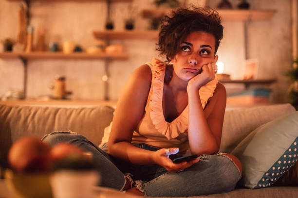 gelangweilte frau, die auf dem sofa sitzt und das telefon hält - mobile phone telephone frustration women stock-fotos und bilder