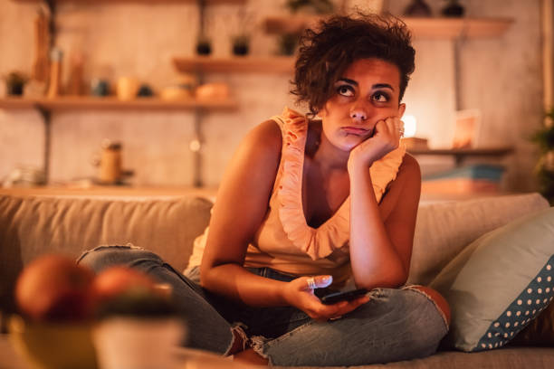 Bored woman sitting on sofa and holding phone Relationship problems, bad news, bored at home with modern gadget. Sad cute millennial woman looking at smartphone, sitting on couch alone in living room interior, indoors. relationship breakup stock pictures, royalty-free photos & images