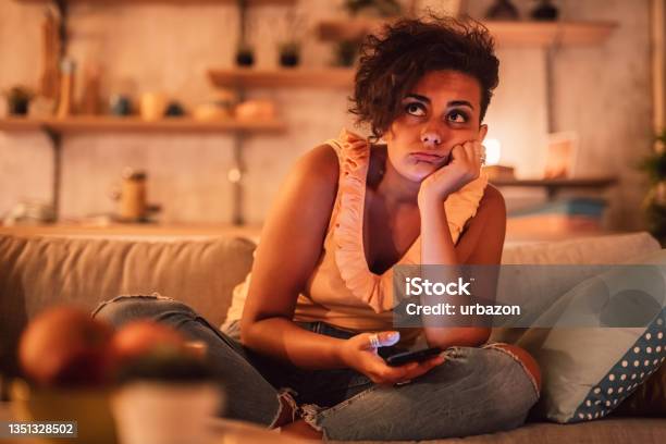 Bored Woman Sitting On Sofa And Holding Phone Stock Photo - Download Image Now - Boredom, Relationship Breakup, Sofa