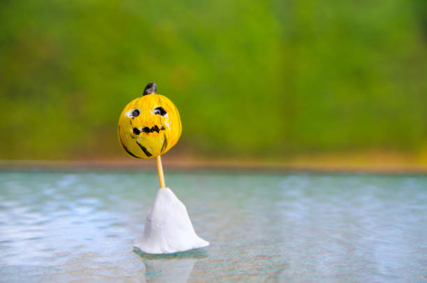 Modelling clay of a pumpkin made by a kid hel by a toothpick and standing on a glass table