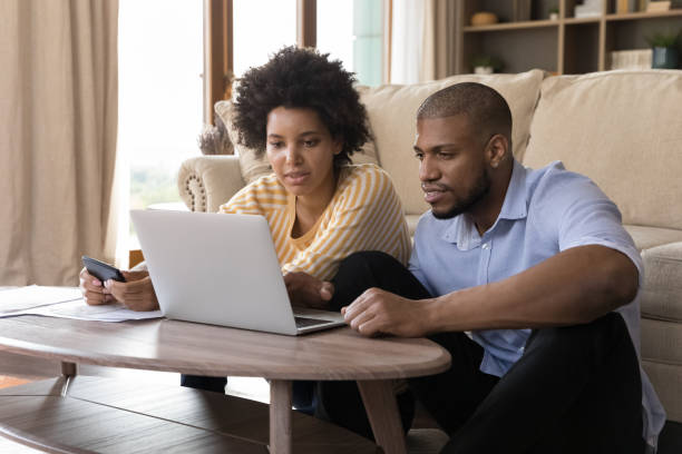 pareja afroamericana joven concentrada que maneja pareja. - home finances couple computer african ethnicity fotografías e imágenes de stock