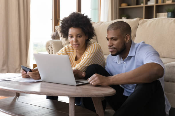 Concentrated young african american couple managing couple. Concentrated young african american married couple looking at computer screen, analyzing household budget, paying bills in e-banking app, planning investment or managing budget together at home. two parents stock pictures, royalty-free photos & images