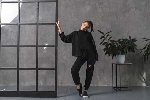 Young woman in black sportswear, pants and sweatshirt. Concept of fashionable sport outfit, indoors photo. Copy space. The concept of sports, healthy lifestyle, fitness, stretching