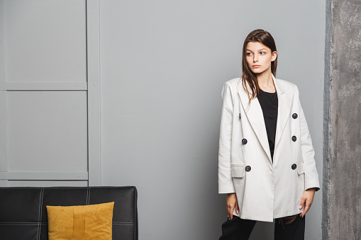 Young elegant woman in white oversize blazer and black ripped pants. Interior portrait.