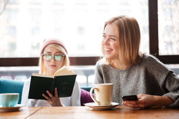 istock Young women friends reading book and drinking coffee. 1351335293