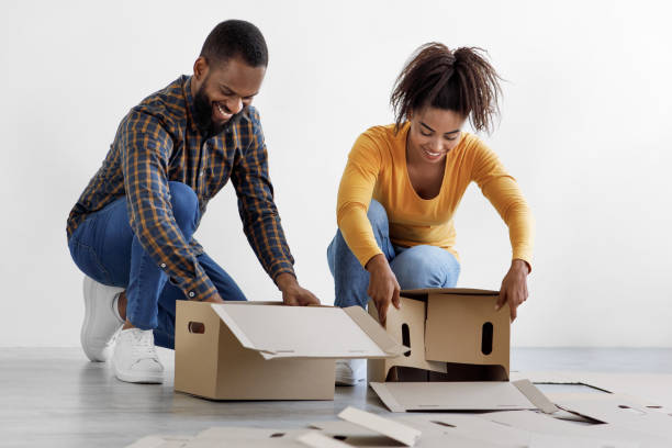 istock Positive young african american husband and wife stack cardboard boxes for moving on floor in empty room 1351335565