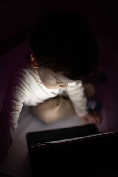 istock Little boy sitting in the dark room and using digital tablet 1351336608