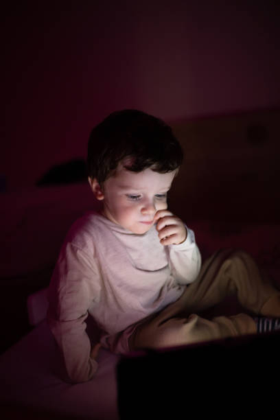 istock Little boy sitting in the dark room and using digital tablet 1351336707