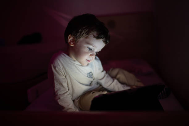 istock Little boy sitting in the dark room and using digital tablet 1351336731