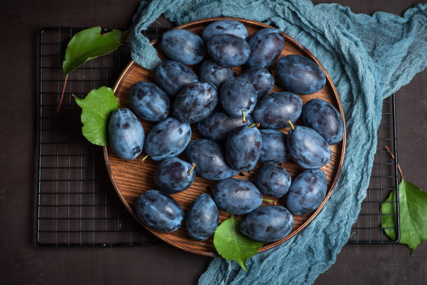 Fresh, organic plums Fresh, organic plums in a beautiful wooden bowl on a brown wooden background. Healthy organic fruit full of vitamins and minerals. Top view plum stock pictures, royalty-free photos & images