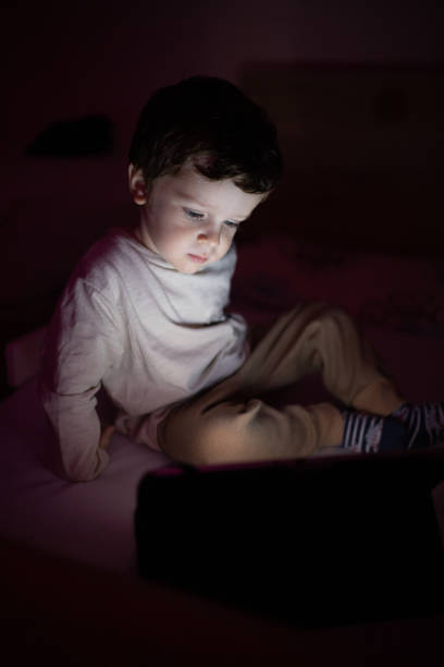 istock Little boy sitting in the dark room and using digital tablet 1351336861