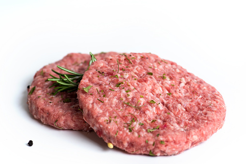 Two raw burgers with fresh spices on a white background isolated.